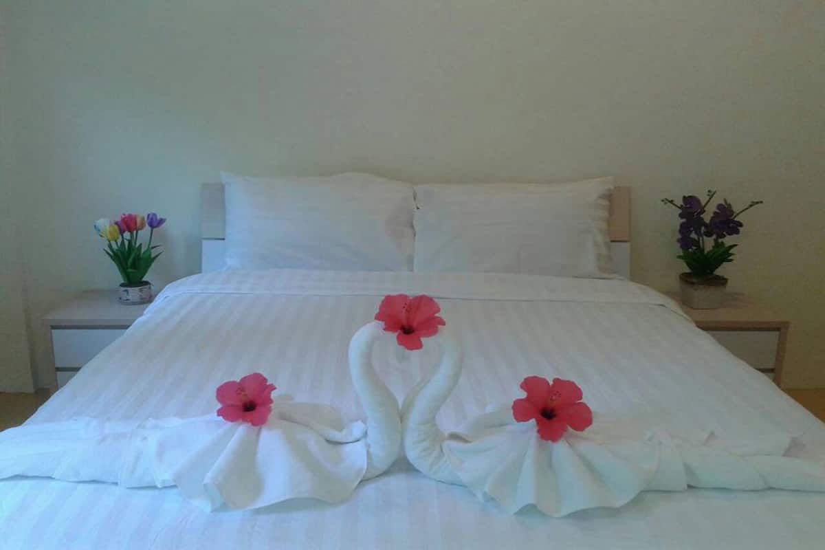 A neatly made bed with white linens and decorative swan shapes made from towels, accompanied by pink flowers.
