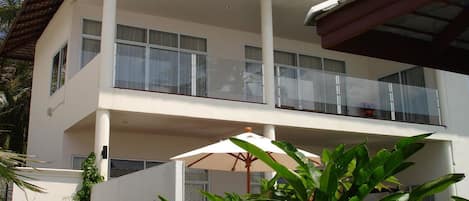 Un edificio de dos pisos con balcones, ventanas amplias y fachada blanca.