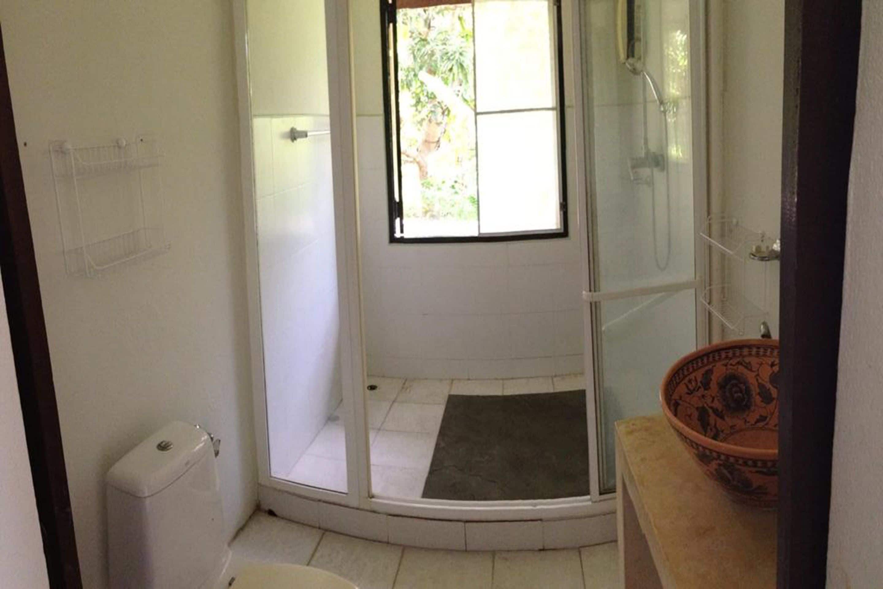 Un baño con cabina de ducha de vidrio, inodoro y lavabo con un recipiente decorativo.