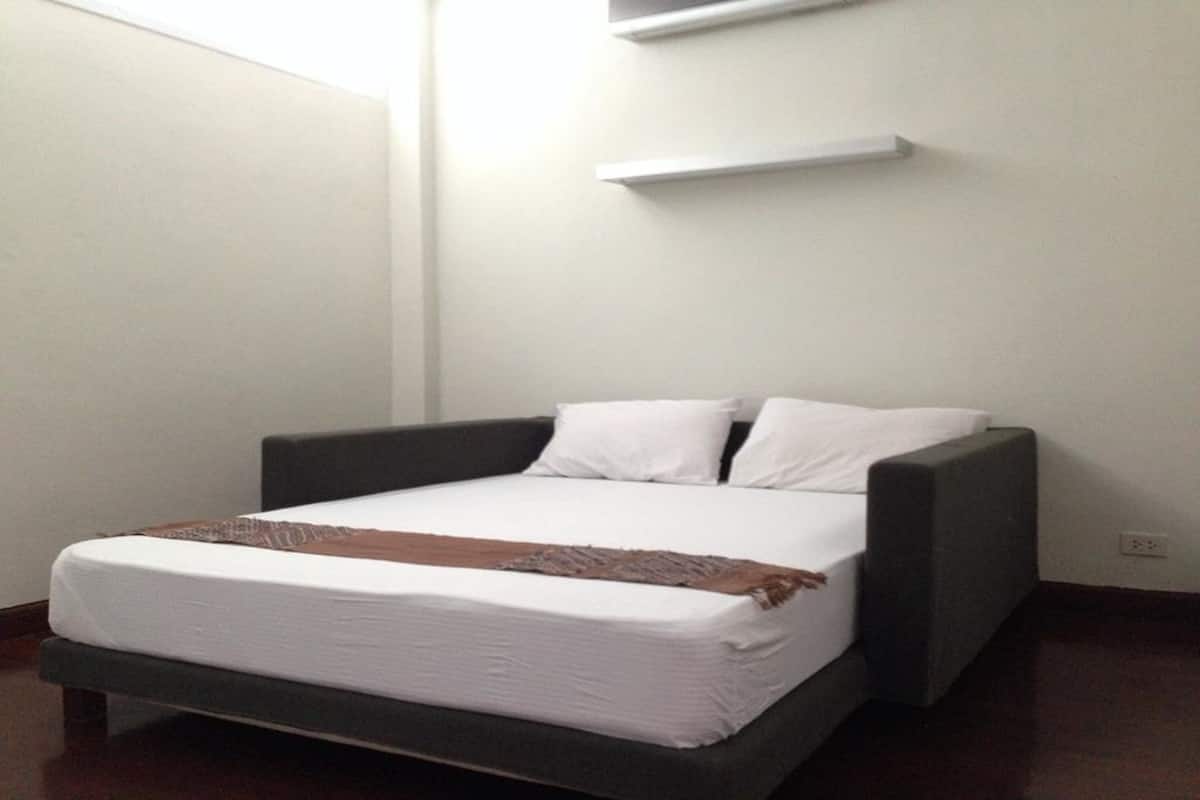 A modern bedroom with a bed, a dark headboard, and a white wall.