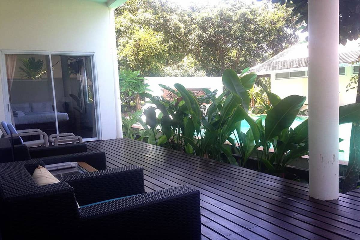 A covered outdoor seating area with wicker furniture and a view of a house and lush greenery.