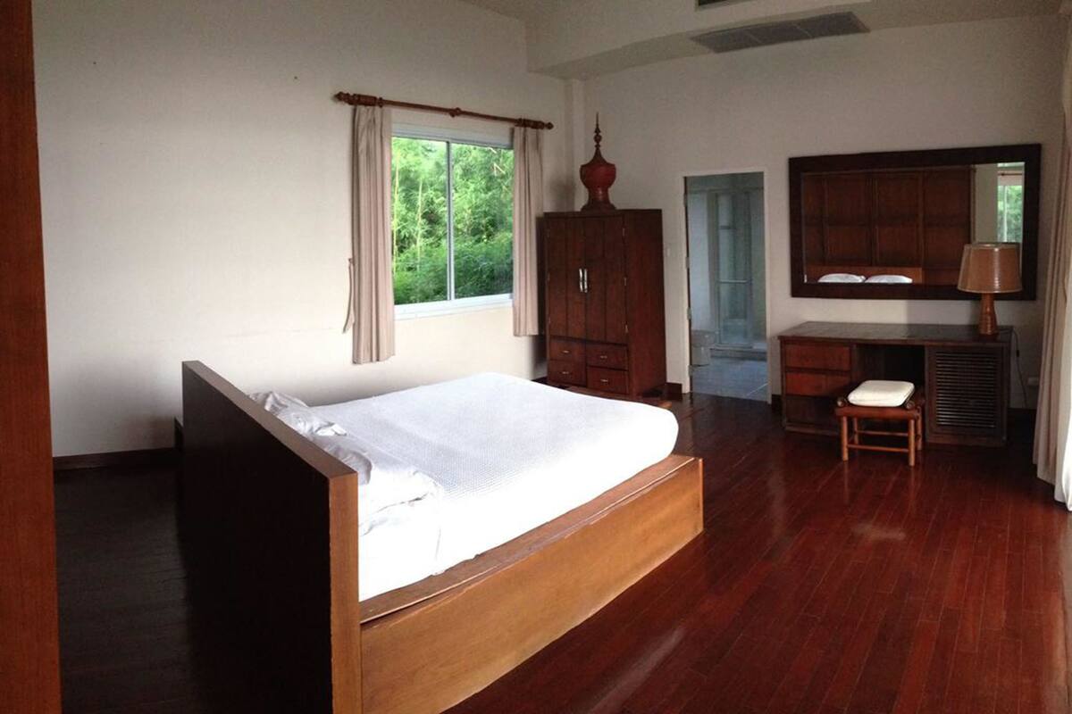 A bedroom with a wooden bed, a wardrobe, a desk with a chair, and a window with curtains.