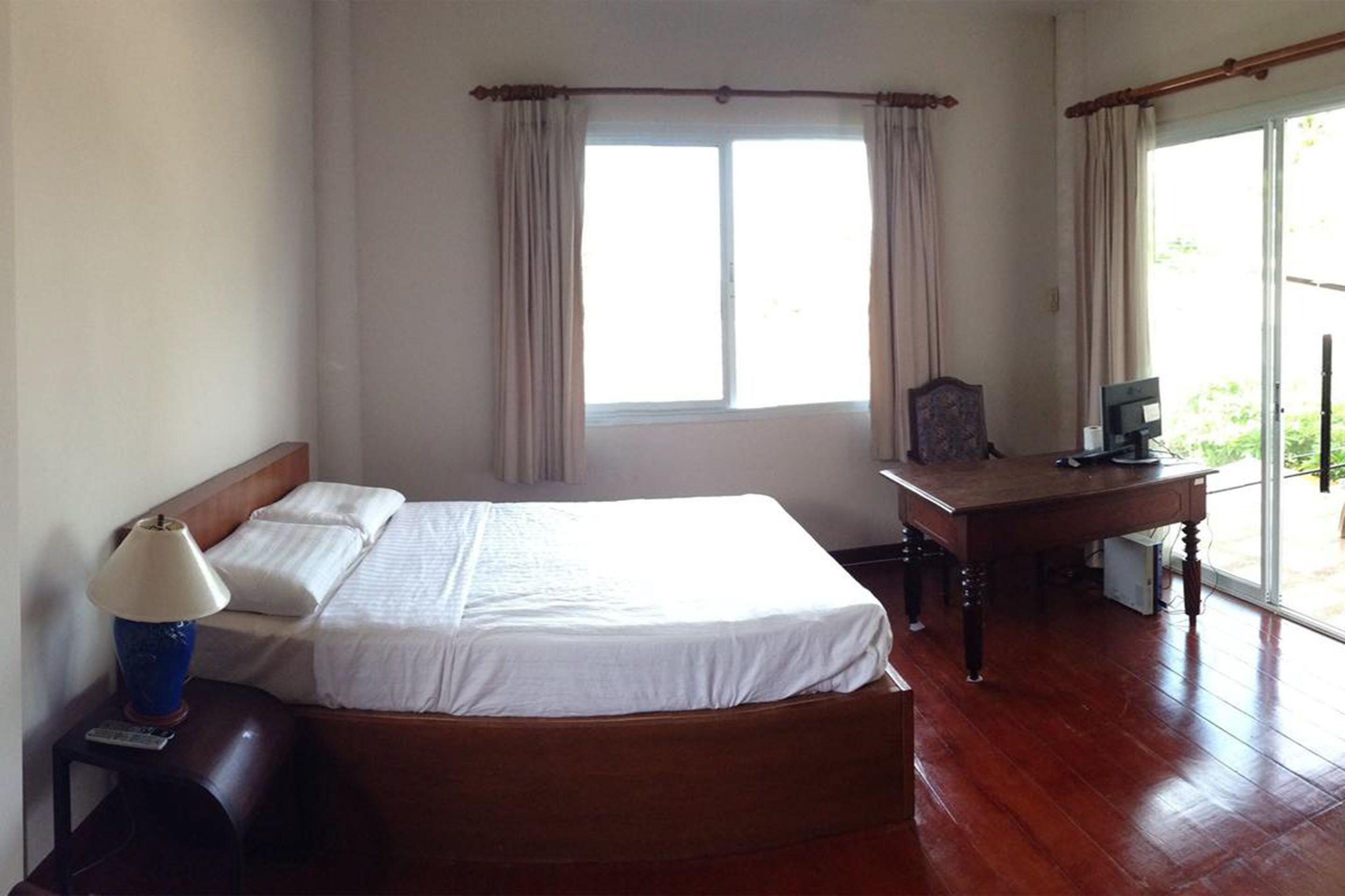 A hotel room with a bed, a desk, a lamp, and a window with curtains.