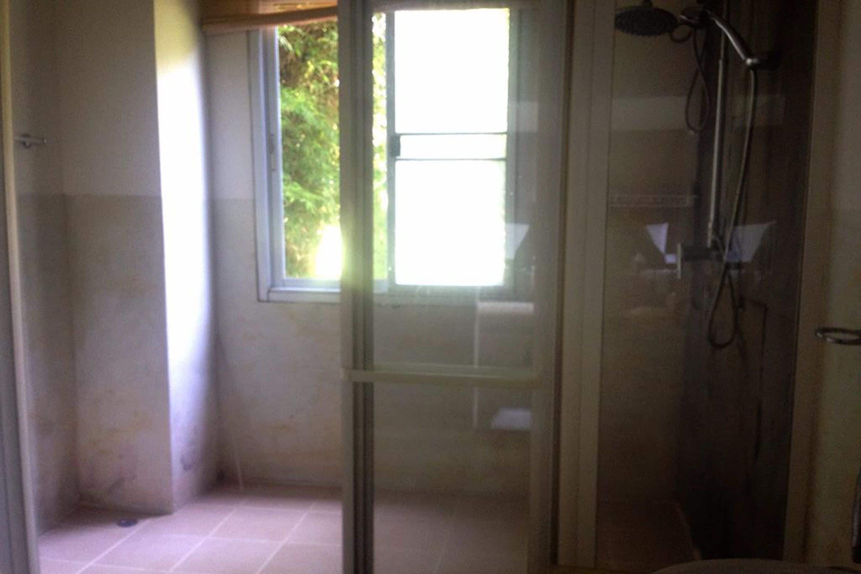 A bathroom with a glass shower enclosure, a window, and a visible showerhead.