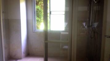 A bathroom with a glass shower enclosure, a window, and a visible showerhead.