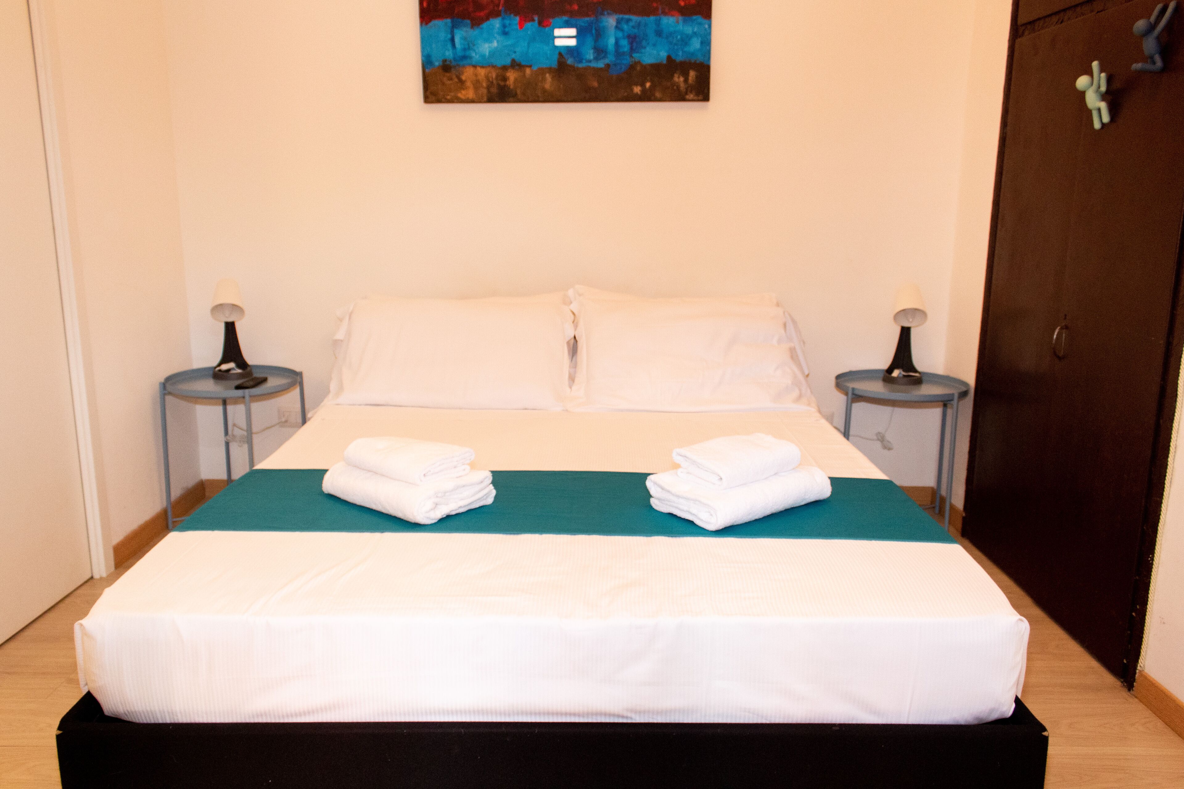 Una cama bien hecha con ropa blanca, dos mesitas de noche con lámparas, y un cuadro en la pared.