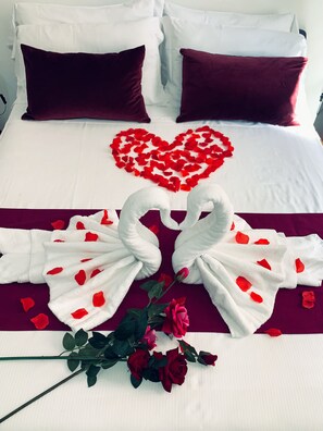 A neatly made bed with a heart-shaped arrangement of rose petals, two towels shaped like swans, and a bouquet of red roses. - ArtHouse (Rome)