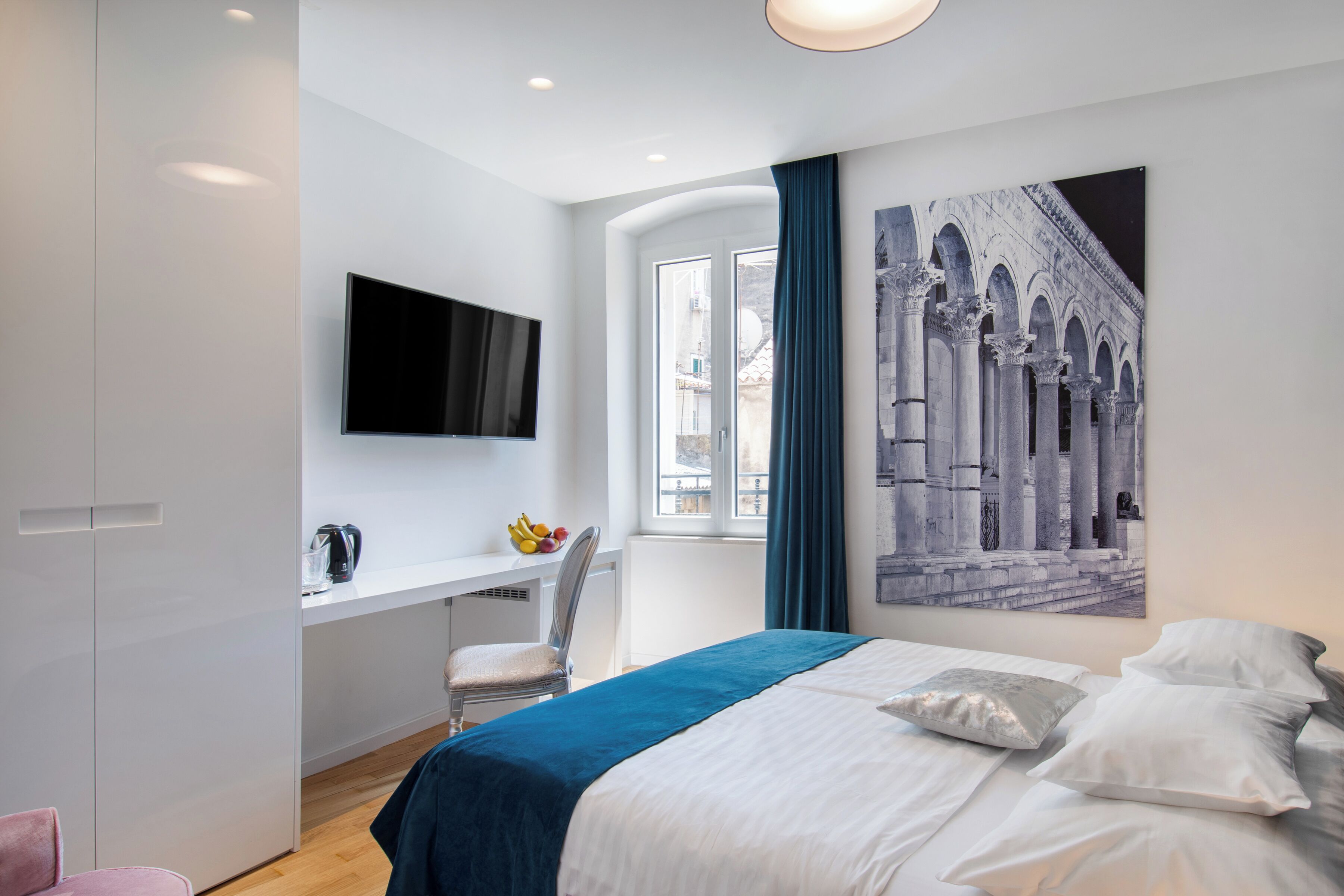 Een moderne hotelkamer met een bed, een bureau, een stoel, een televisie en een raam met uitzicht op een gebouw.