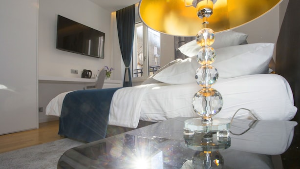 A modern hotel room with a large bed, a glass coffee table, a flat-screen TV, and a view of the city through the window. - Luxury rooms Paula (Split)