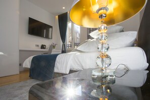 A modern hotel room with a large bed, a glass coffee table, a flat-screen TV, and a view of the city through the window. - Luxury rooms Paula (Split)