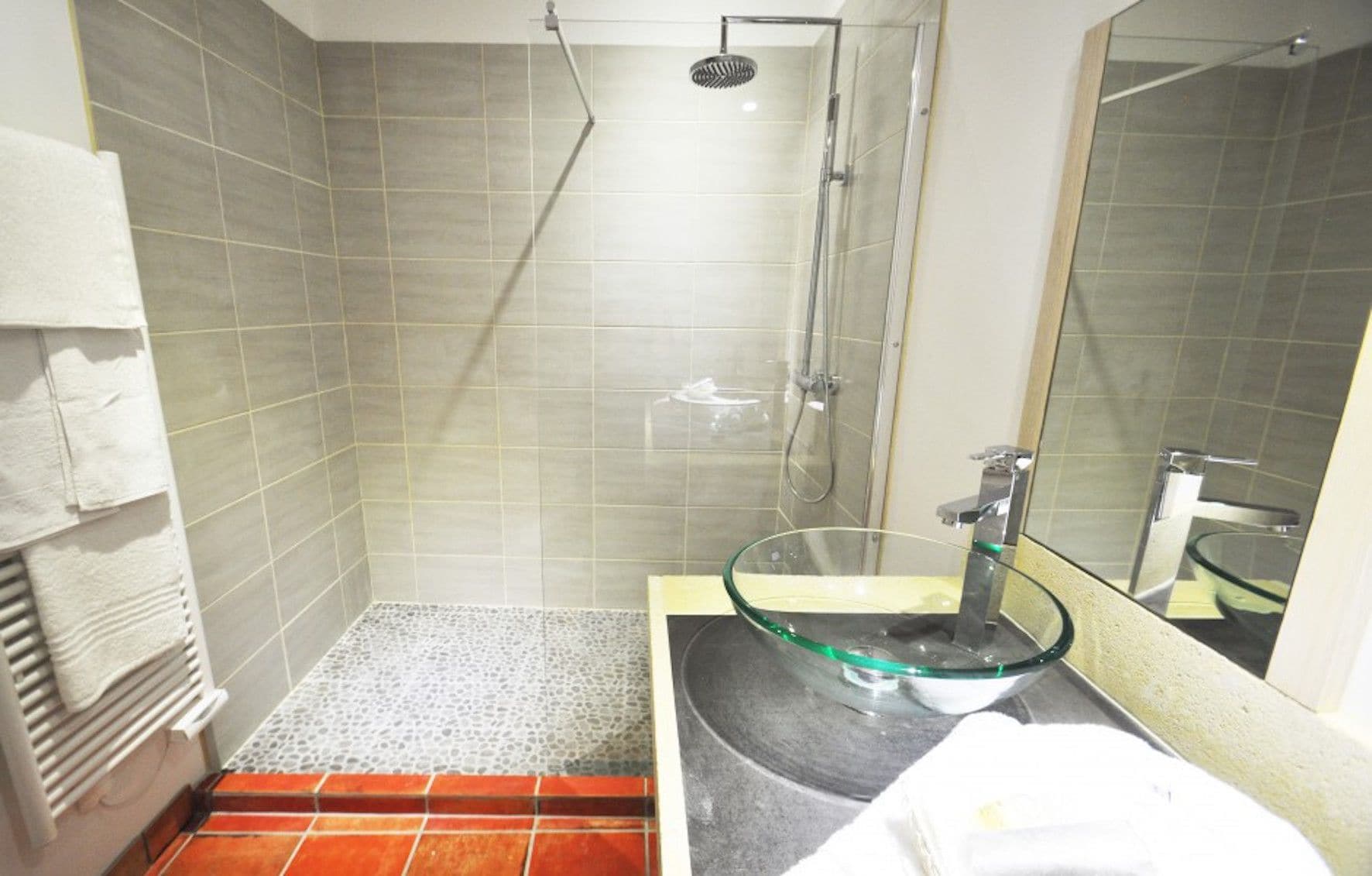 Casa de banho com lavatório de vidro, chuveiro e chão em mosaico.