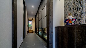 A hallway with a dark wooden panel and a decorative figure on a stand. - RESI STAY Yasaka-An (Kyoto)