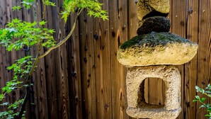 A stone lantern in a garden with a wooden fence in the background. - RESI STAY Yasaka-An (Kyoto)