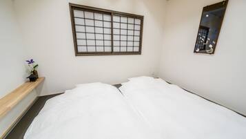 A room with a bed, a window with a grid pattern, a mirror, and a small shelf with a flower.