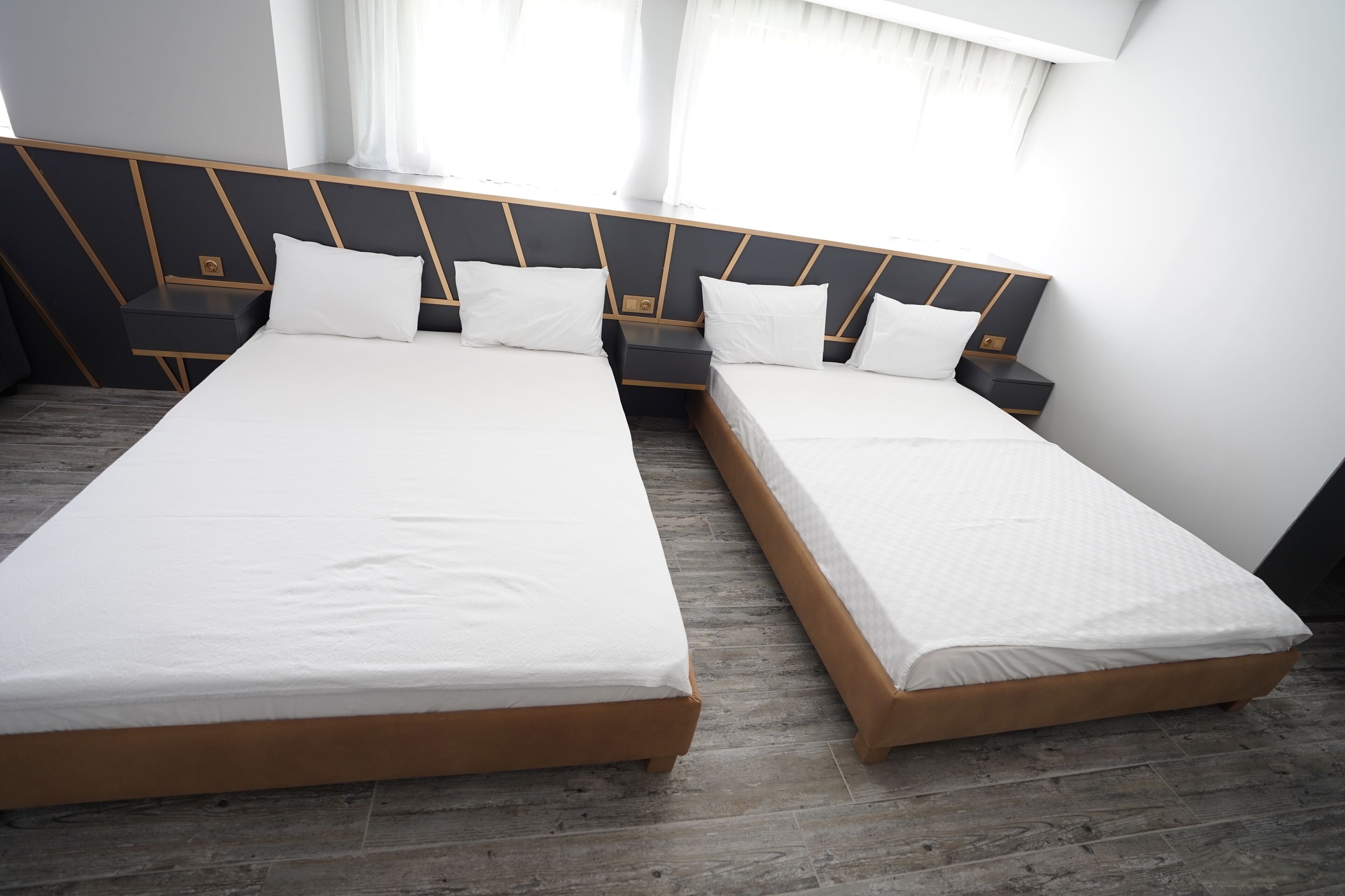 A modern hotel room with two single beds, wooden headboards, and a large window with curtains.