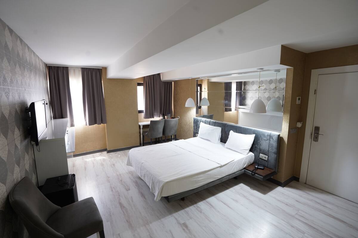 A hotel room with a large bed, a desk, a chair, and a TV.
