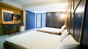 Quarto de hotel com uma cama grande, uma escrivaninha com cadeira, uma TV de tela plana na parede e uma janela com persianas.