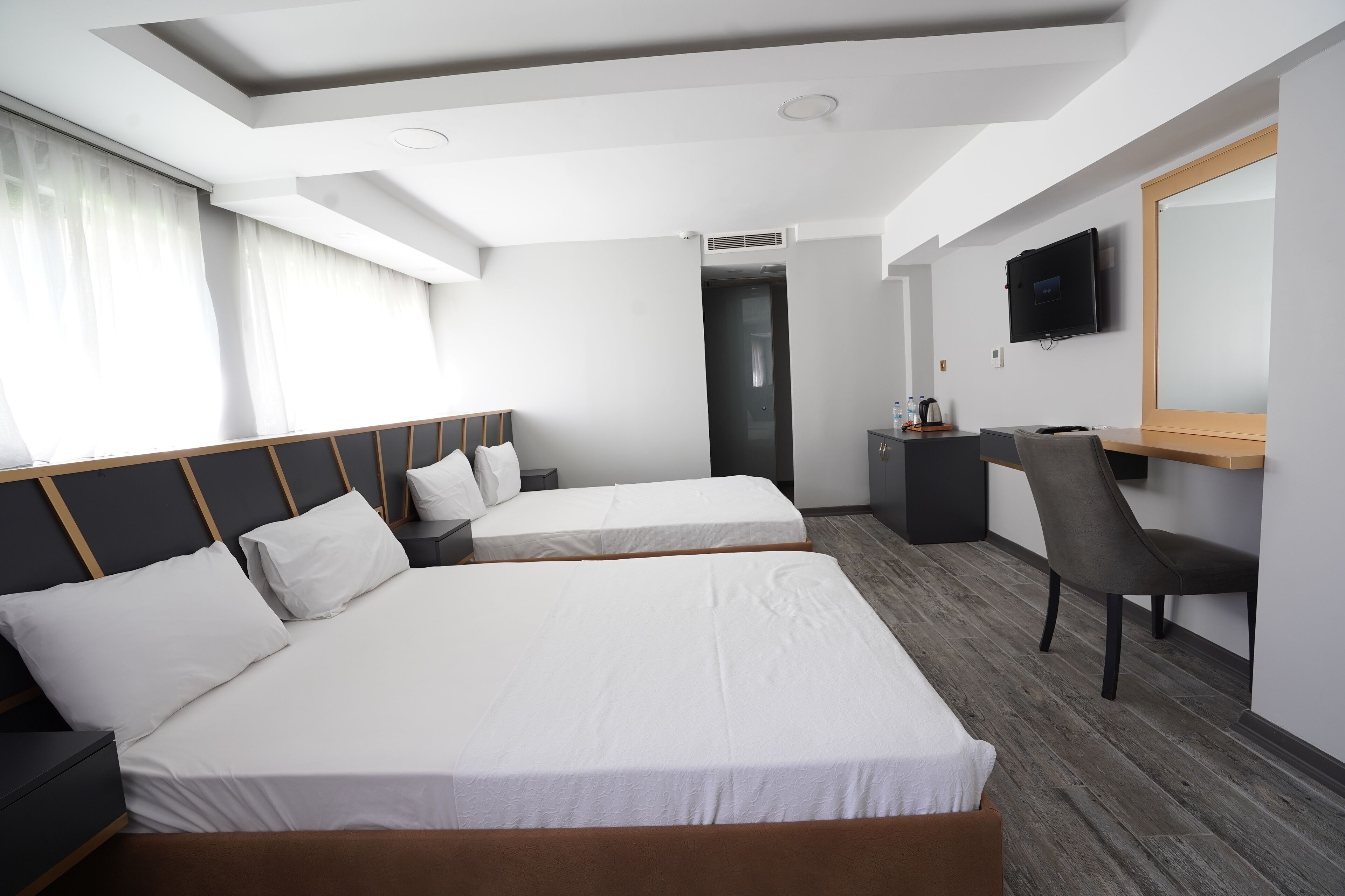 A hotel room with two beds, a desk, a chair, and a TV on the wall.