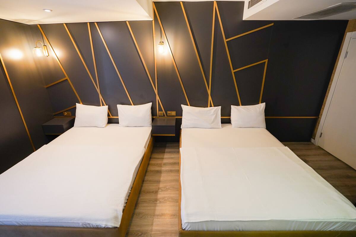 A modern hotel room with two beds, wooden flooring, and geometric wall design.