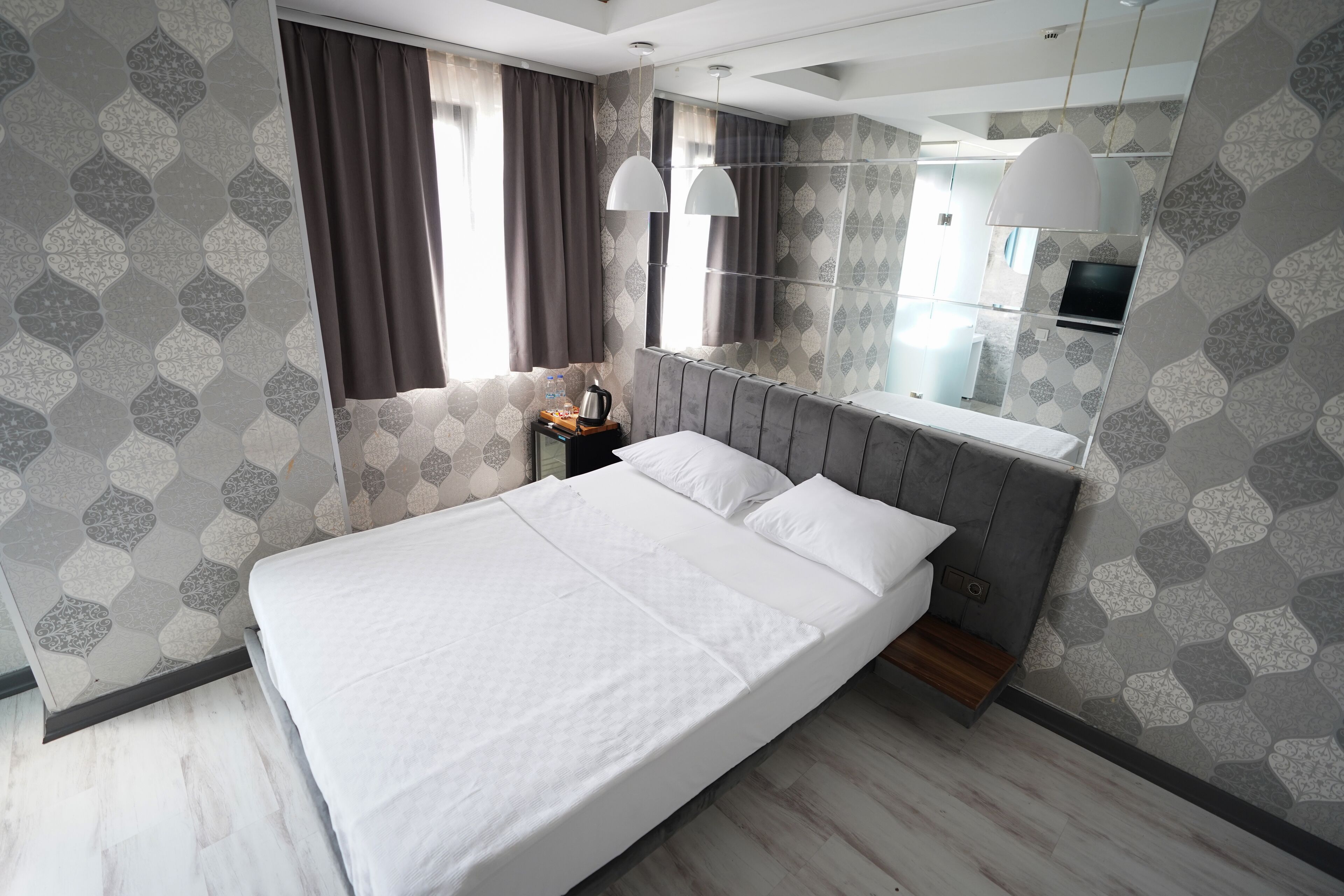 Una habitación de hotel moderna con una cama grande, una mesita de noche con lámpara, un espejo y papel tapiz estampado.
