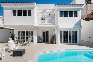 A two-story white house with a swimming pool, outdoor seating, and a balcony.