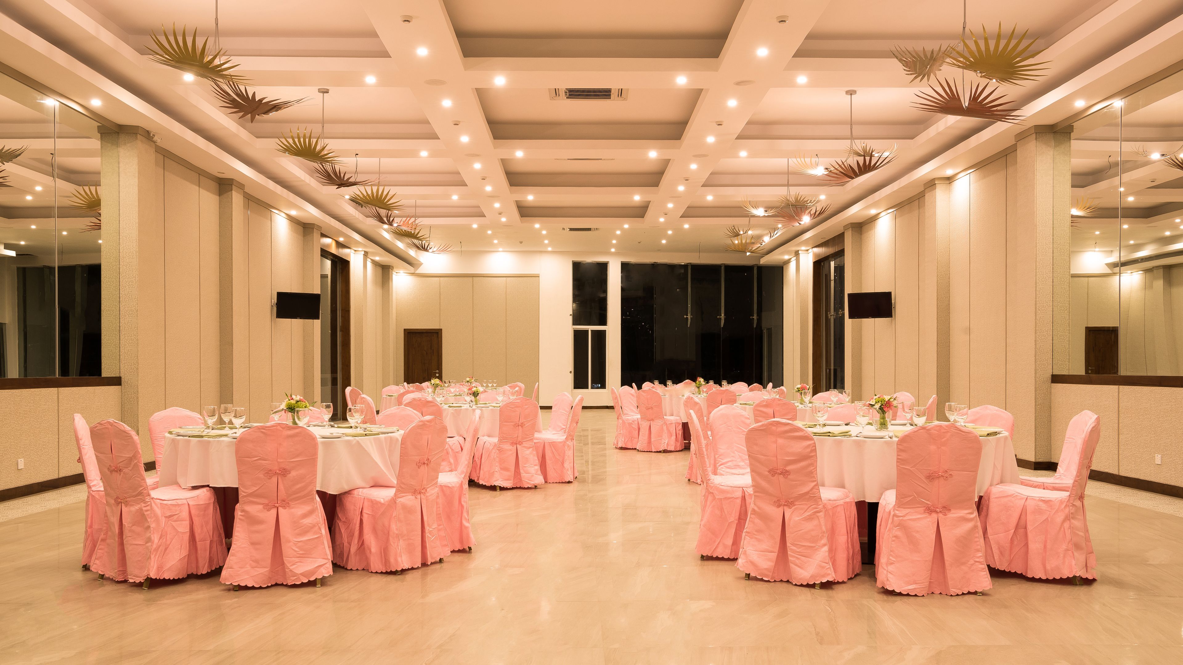 A banquet hall with round tables, pink chairs, and ceiling lights.