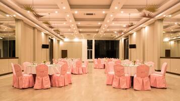 A banquet hall with round tables, pink chairs, and ceiling lights.