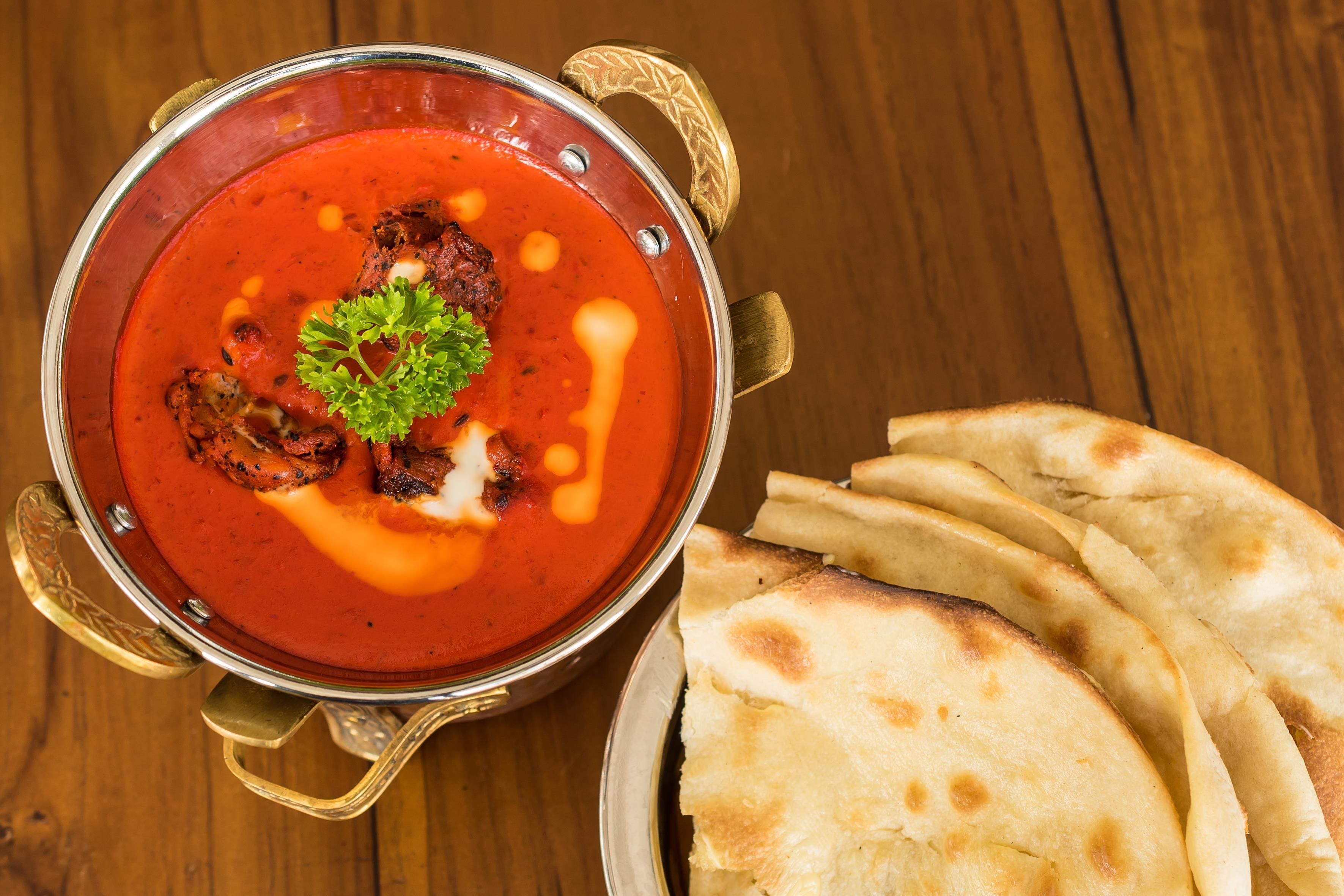 A bowl of red soup garnished with a sprig of parsley and a dollop of cream, accompanied by flatbreads on a wooden table.