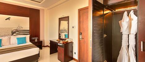 A bedroom with a bed, a desk, a mirror, and a walk-in closet with hanging robes.