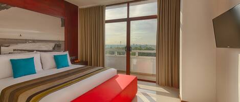 A hotel room with a large bed, a red accent wall, a balcony with a view, and a flat-screen TV.