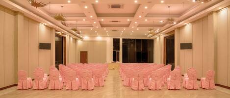 A conference room with rows of pink chairs, a stage, and a ceiling with recessed lighting and decorative elements.