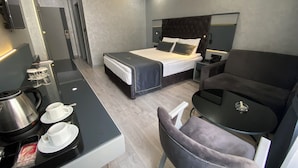 A modern hotel room with a bed, a desk with a coffee maker, a chair, and a small table. - Alfin Hotel Ankara (Ankara)