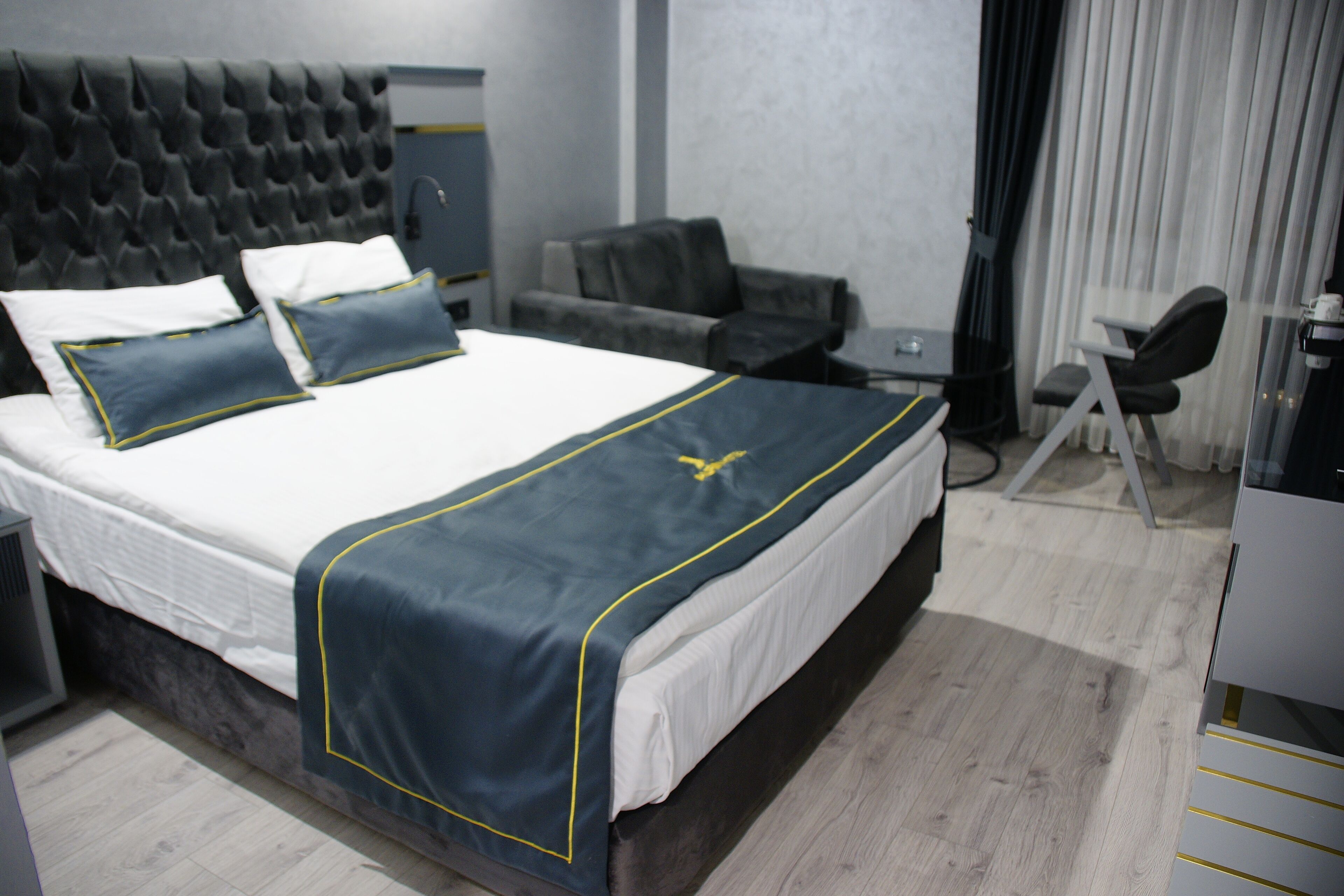 A hotel room with a large bed, a tufted headboard, a desk, a chair, and a sofa.