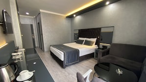 A modern hotel room with a bed, a desk with a coffee maker, a chair, and a small table. - Alfin Hotel Ankara (Ankara)