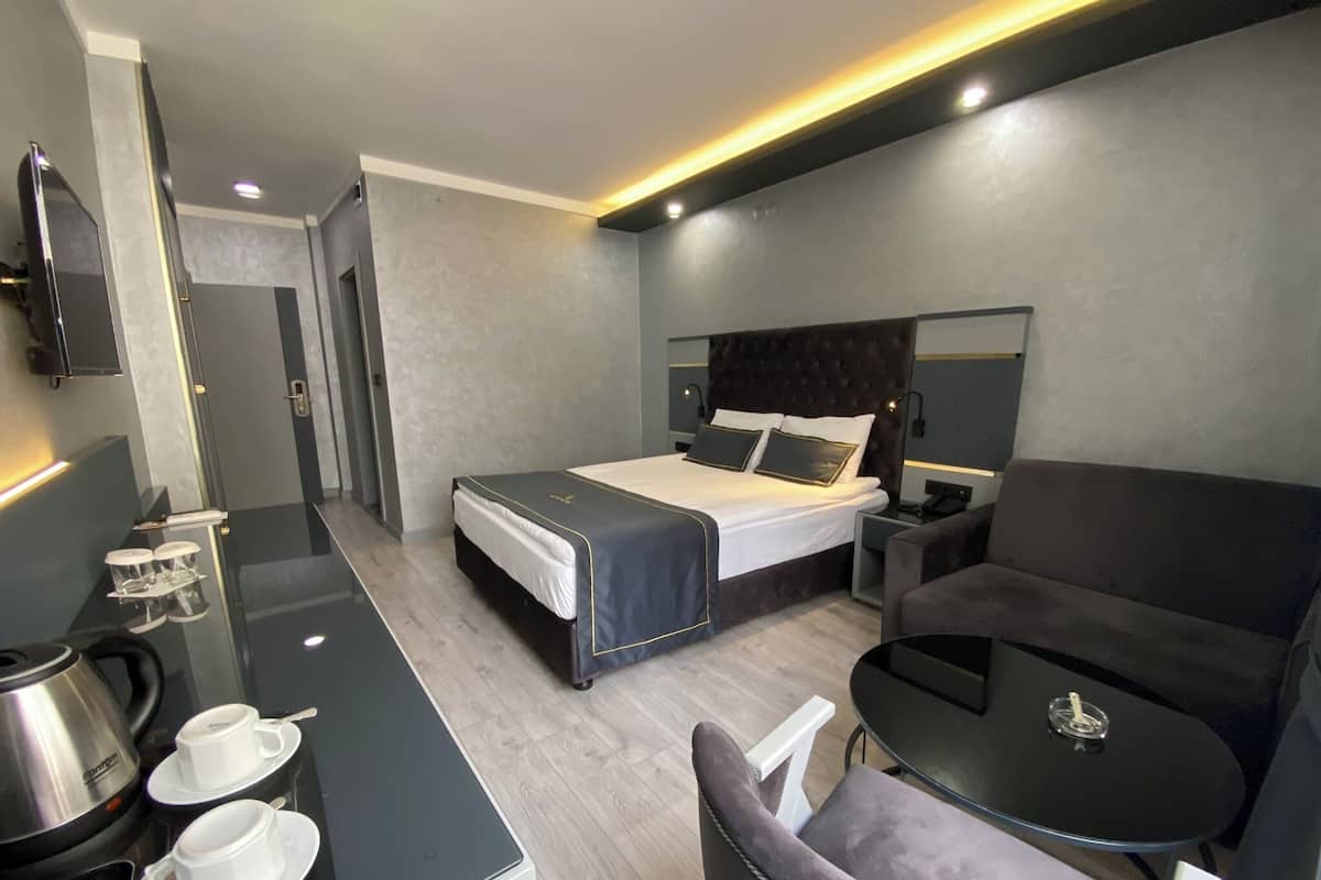 A modern hotel room with a bed, a desk with a coffee maker, a chair, and a small table.