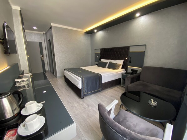 Una habitación de hotel moderna con una cama, un escritorio con cafetera, una silla y una mesita.