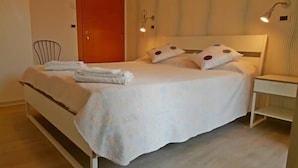 A neatly made bed with pillows and a folded towel, a bedside table, and a chair in a room with a wooden floor and a door in the background. - Hotel St. Moritz (Rimini)