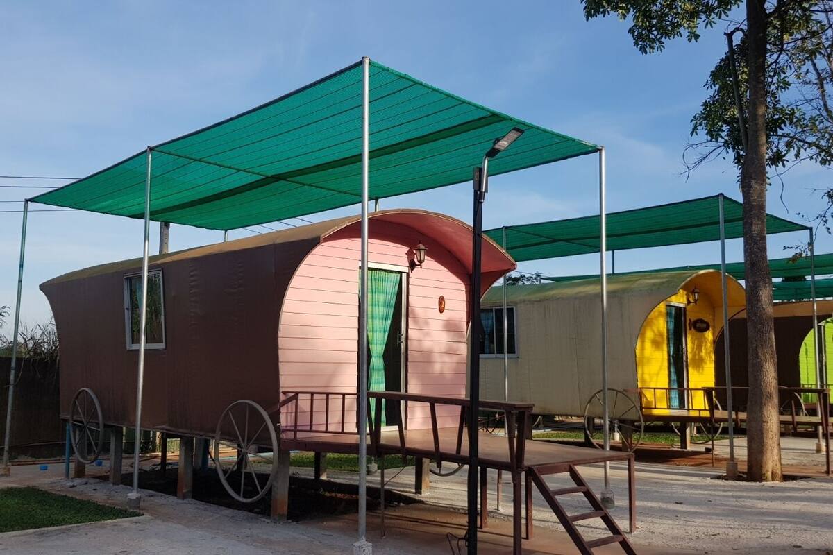 Een rij klassieke caravans, elk met een groen dakzeil, een klein terrasje en een raam.