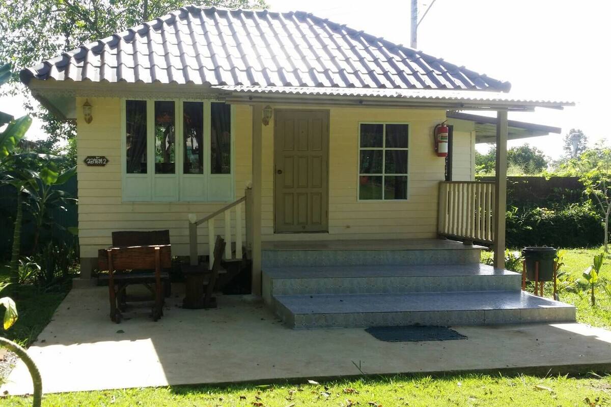 Een klein, laag huis met een pannendak, een veranda en een kleine voortuin.