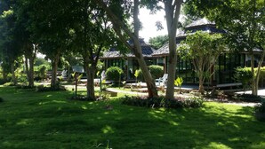 Un jardín bien cuidado con árboles, césped y un edificio tradicional con tejado de tejas.