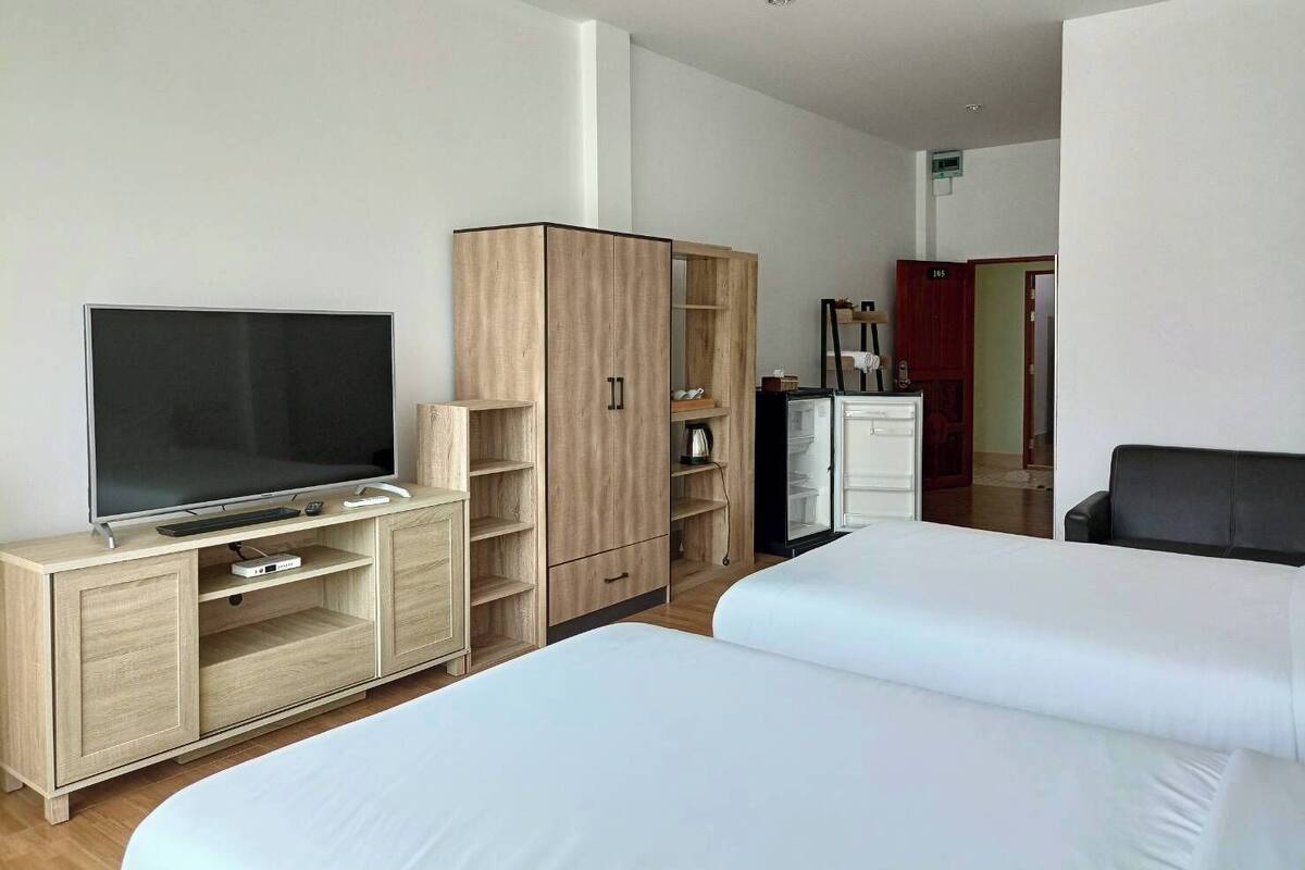 Een hotelkamer met een televisie, een houten garderobe, twee bedden en een koelkast.