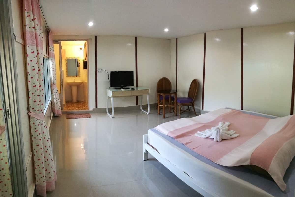 Een slaapkamer met een bed, een bureau, twee stoelen, een televisie en een badkamer zichtbaar door een geopende deur.