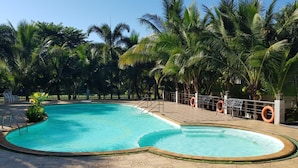 Una piscina de borde curvo, rodeada de palmeras y una cerca con flotadores salvavidas.
