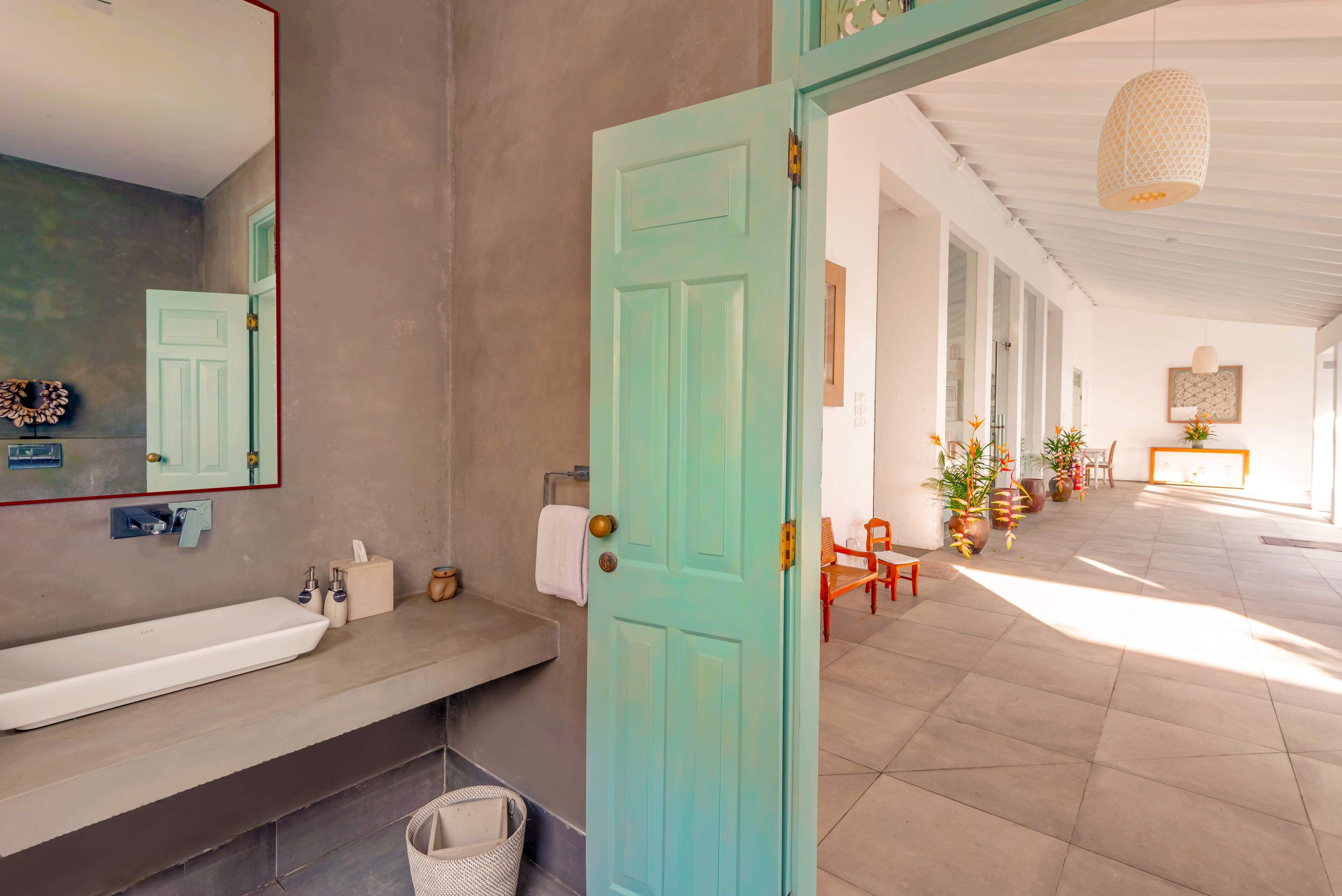 Un baño con un lavamanos grande de color blanco, un espejo y una puerta color verde azulado.