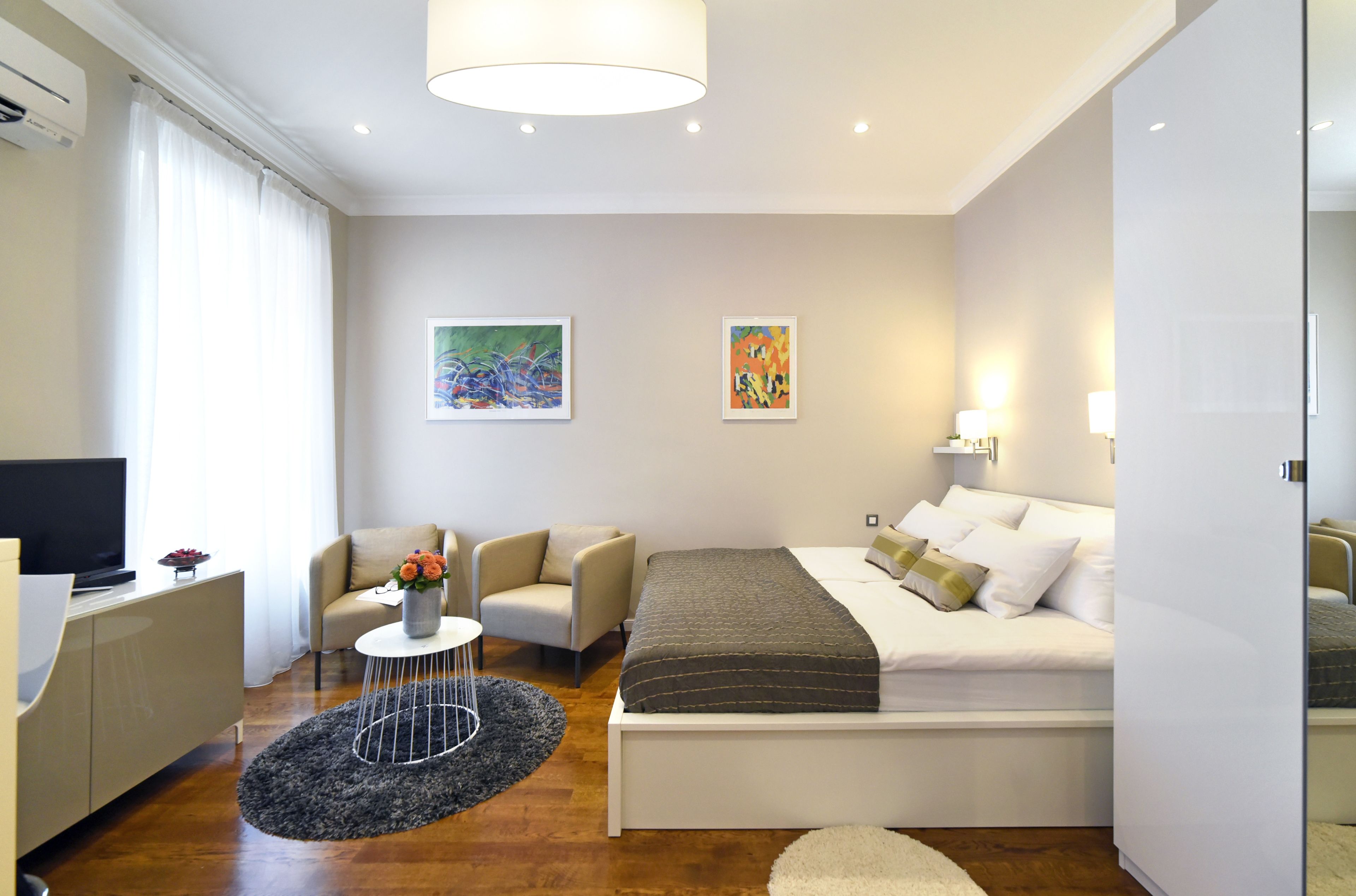 A modern hotel room with a bed, a sofa, a TV, and artwork on the walls.