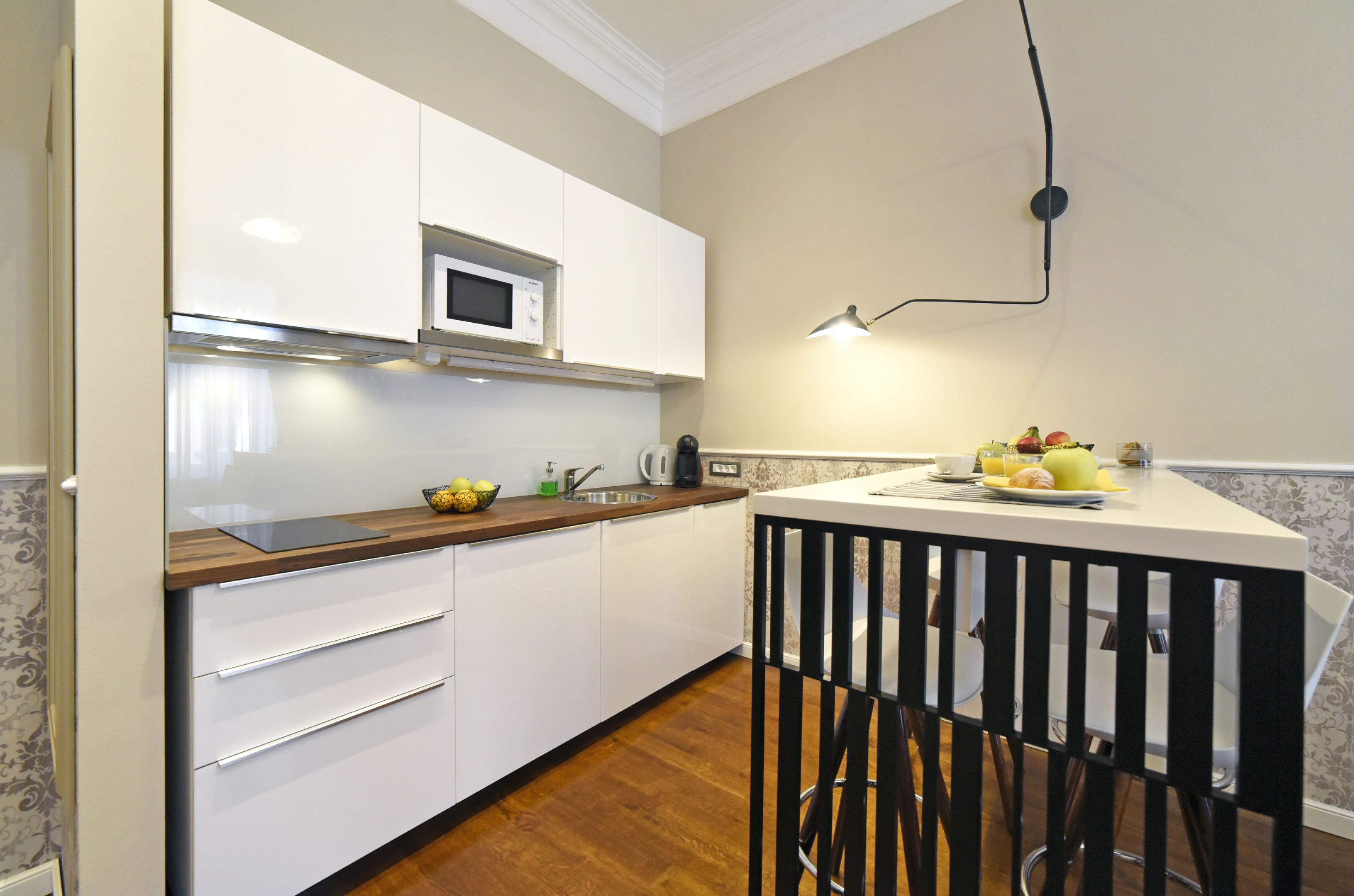 A modern kitchen with white cabinets, a microwave, a sink, and a dining area with a black chair.