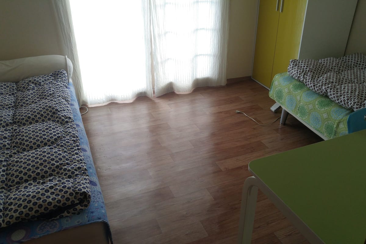 A room with two beds, a wooden floor, a yellow wardrobe, and a green desk.