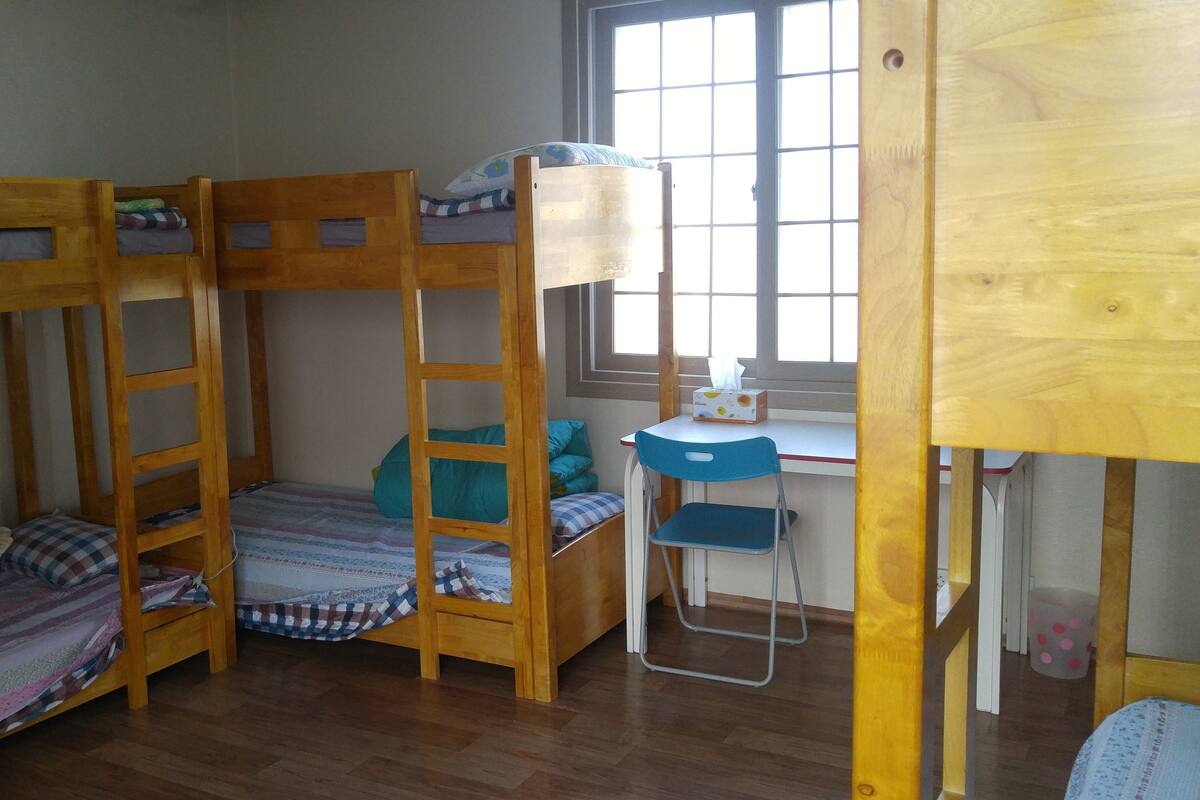 A bunk bed room with a desk and chair, a window, and a trash bin.