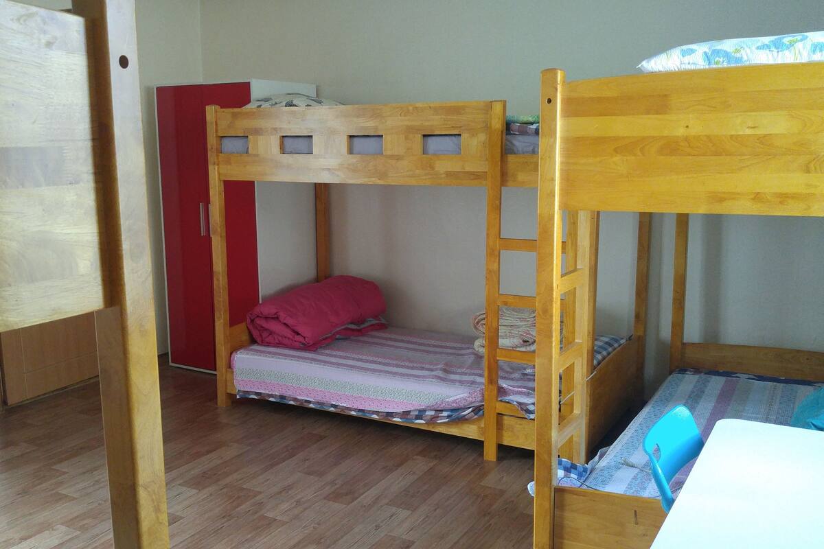 A bunk bed room with a wooden floor, a red wardrobe, and a bed with a patterned bedspread.