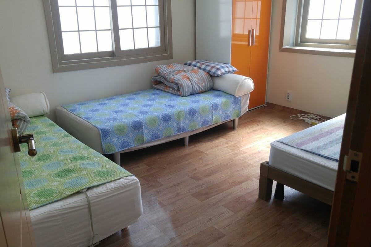 A small, well-lit room with two single beds, a wooden floor, and a window providing natural light.